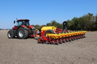 Červený traktor táhne žlutočervený přesný secí stroj Väderstad na poli.