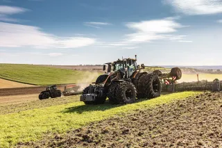 Tmavý traktor Valtra série S s nářadím při práci na poli