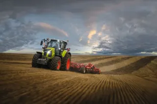 Traktor Claas s podmítačem na poli za soumraku