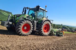 Zelený traktor Fendt se zemědělským nářadím na poli
