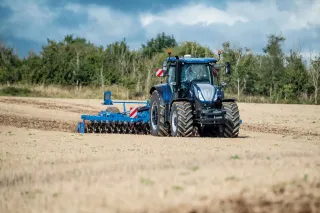 Modrý traktor New Holland T7 s diskovým nářadím na poli