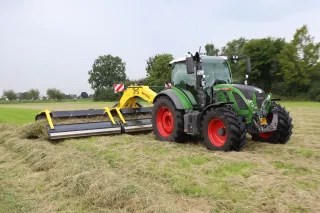 Zelený traktor Fendt se žlutým pásovým shrnovačem Kverneland ROC na louce