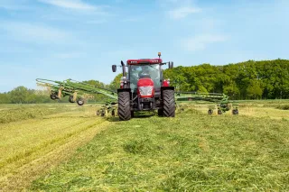 Červený traktor s rozloženým shrnovačem Krone Swadro na louce