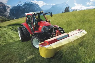 Červený traktor Lindner se žacím strojem na horské louce