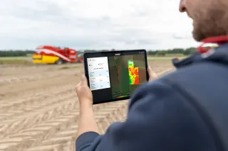 Muž drží tablet s mapou výnosů Grimme CropAnalyser před sklízecím strojem