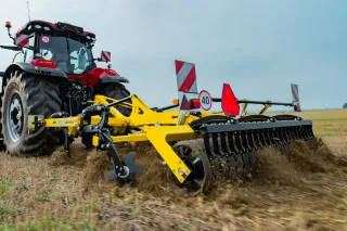 Traktor s neseným žlutým kypřičem BEDNAR FENIX při práci na poli