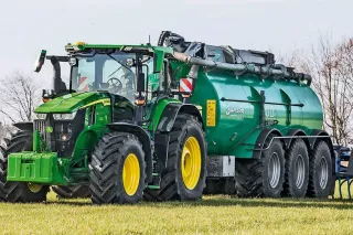 Zelený traktor John Deere s cisternou na poli