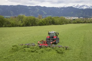 Traktor s červeným shrnovačem na louce pod horami
