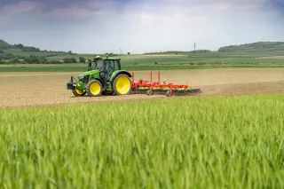 Zelený traktor táhne červené prutové brány Pöttinger po poli