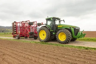 Traktor John Deere s červeným kypřičem Horsch na polní cestě