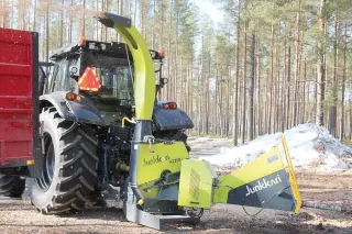 Žlutozelený štěpkovač Junkkari připojený k traktoru v lese
