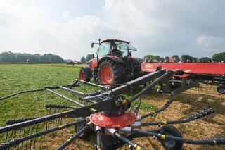 Traktor s obracečem sena na travnatém poli.
