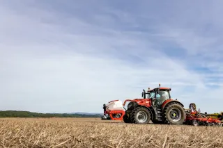 Červený traktor se secím strojem SUMO DTS na poli