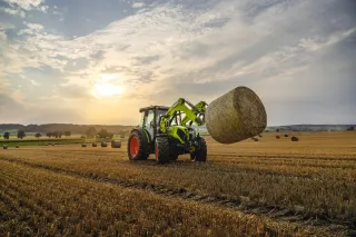 Traktor Claas zvedá čelním nakladačem kulatý balík na poli