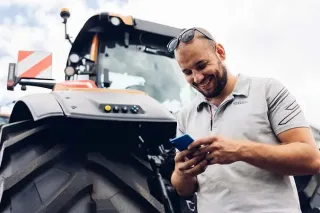Muž používá mobilní telefon vedle traktoru Valtra