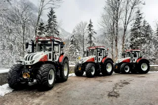 Tři bíločervené traktory Steyr na zasněžené cestě