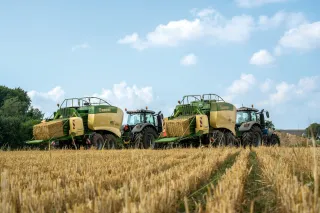 Dva traktory s lisy Krone lisují slámu na poli