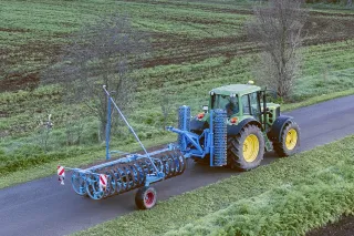 Traktor přepravuje modrý polní pěch Lemken po silnici