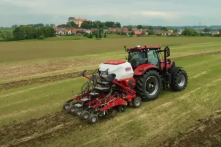 Červený traktor táhne stroj Sumo pro pásové zpracování půdy