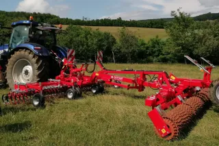Modrý traktor s červeným nářadím Güttler stojí na louce
