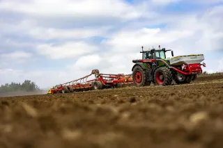 Traktor s červeným podmítačem Pöttinger na poli