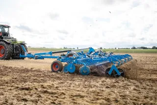 Traktor s modrým diskovým podmítačem Lemken Rubin na poli
