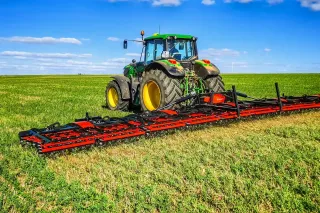 Traktor s širokými prutovými branami Kverneland na poli