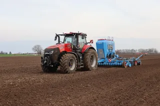 Červený traktor Case IH Magnum 400 táhne modrý secí stroj LEMKEN Solitair DT na poli.