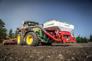 Traktor John Deere se secím strojem Pöttinger na poli
