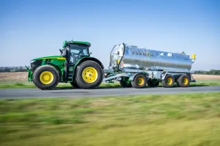 Traktor John Deere táhne stříbrnou cisternu Joskin Tetraliner RL po silnici.