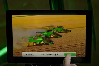 Obrazovka s trojicí sklízecích mlátiček John Deere a výzvou k zahájení sklizně.