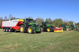 Traktory John Deere se stroji Pöttinger na louce.