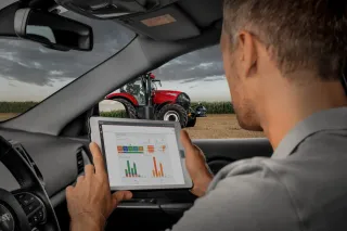 Muž v autě sleduje údaje o traktoru Case IH na tabletu.
