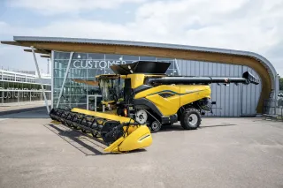 Žlutá sklízecí mlátička New Holland CR10 před budovou.