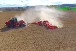 Pásový traktor táhne červený kompaktor SMS SEVERIT G na poli.