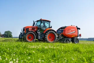 Traktor Kubota s kulatým lisem na louce.