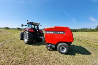Traktor táhne červený lis ROZMITAL na posečené louce.