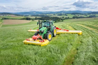 Traktor John Deere se žací trojkombinací Pöttinger na louce.
