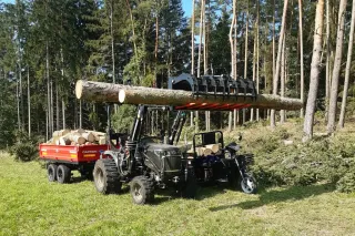 Černý traktor Captain nakládá klády v lese.
