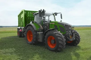 Zelený traktor Fendt s přívěsem na louce.