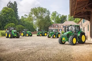 Pět zelených traktorů John Deere před historickou budovou.