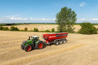 Traktor Fendt s červeným překládacím vozem Perard na strništi.