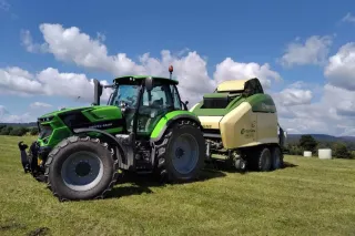 Zelený traktor s lisem Krone na travnatém poli.