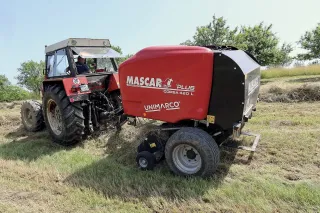 Starší červený traktor s červeným lisem Mascar na louce.