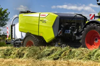 Zelený lis Claas Rollant za traktorem při sklizni trávy.