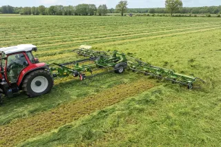 Traktor s obracečem Krone Vendro na louce.