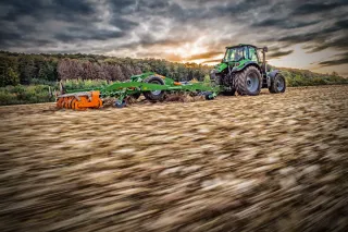 Traktor se zeleným strojem Amazone Ceus na strništi.