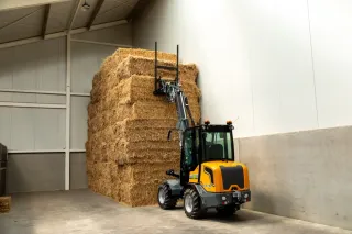 Elektrický teleskopický nakladač GIANT zvedá balíky slámy ve skladu.