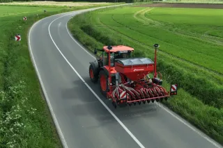Traktor se secím strojem Kverneland Satio projíždí po silnici.