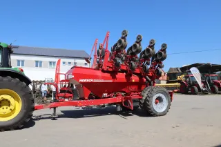 Červený secí stroj Horsch připojený k traktoru na dvoře.